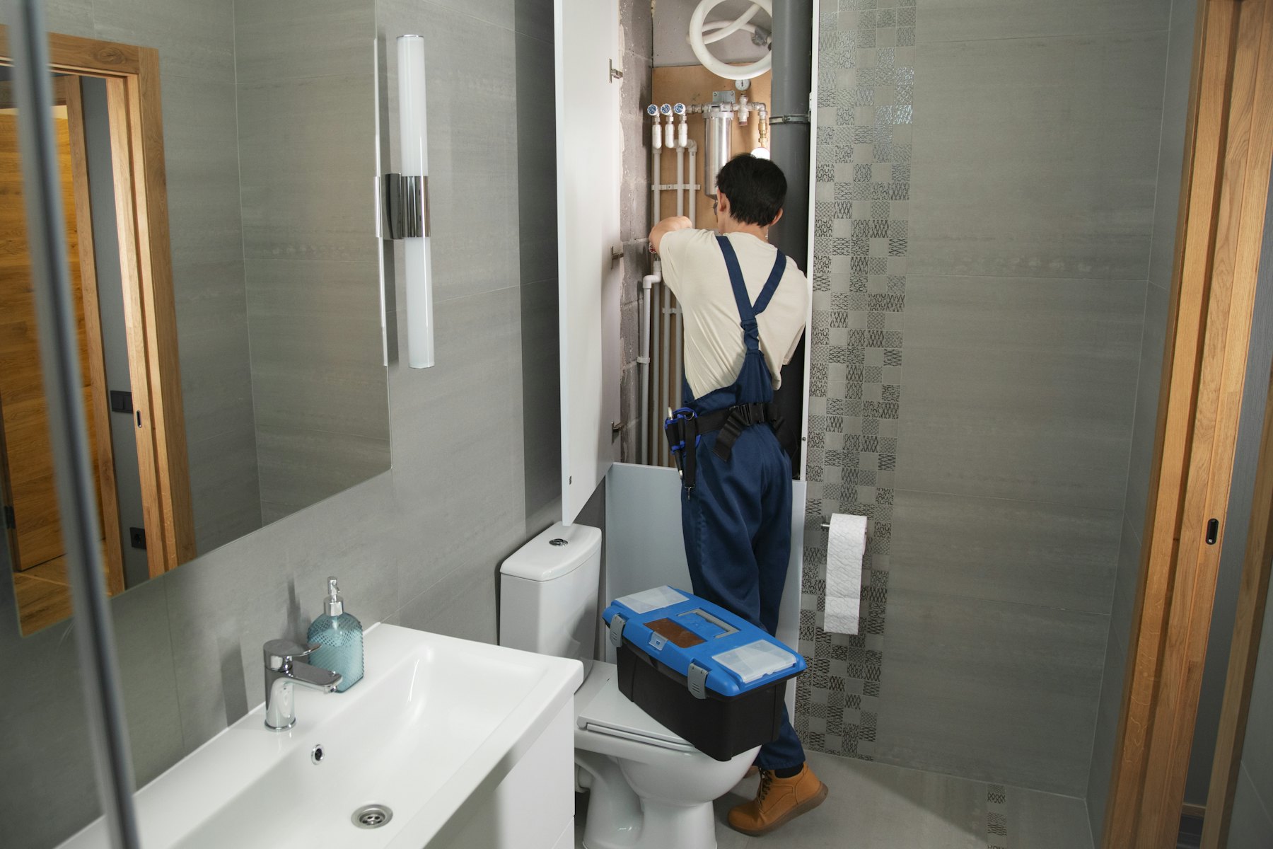 A Hawthorne plumber working on the pipework behind a bathroom wall panel