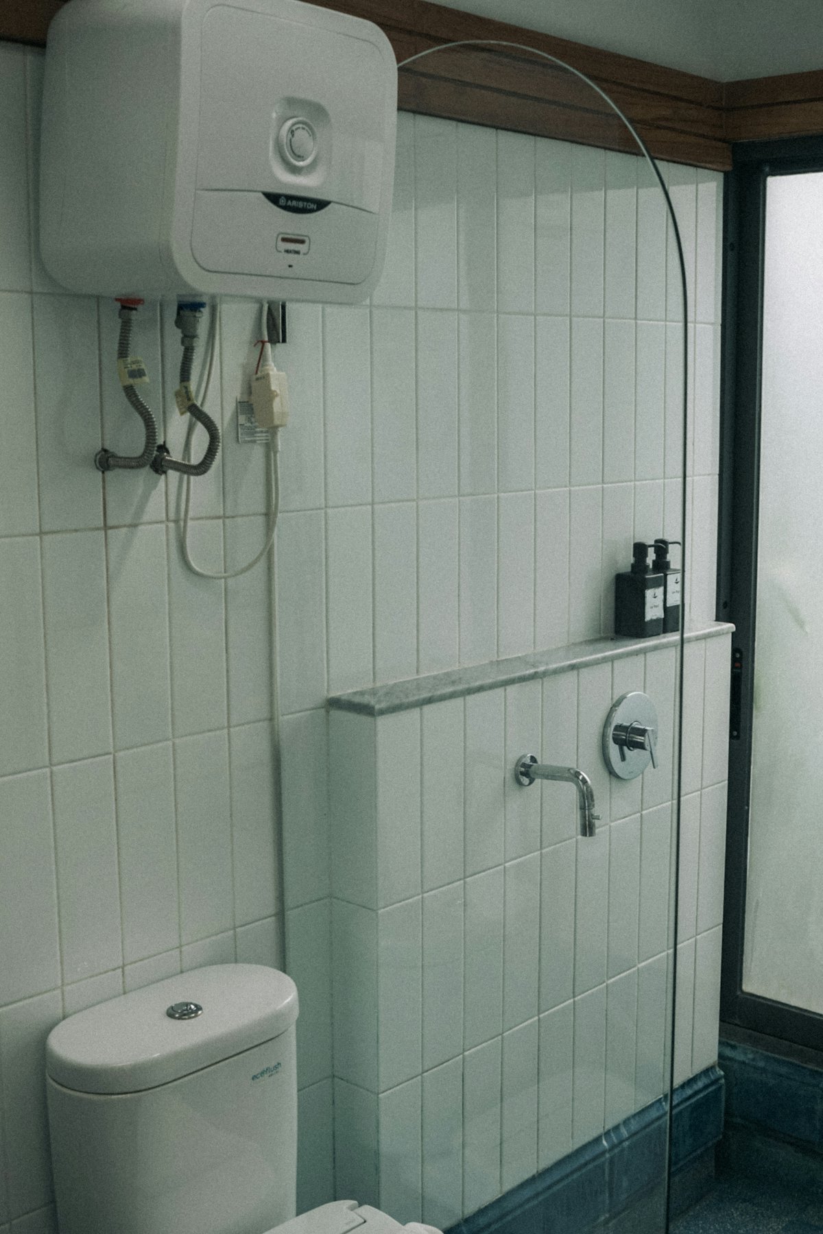 A wall-mounted water heater above a toilet in a tiled bathroom